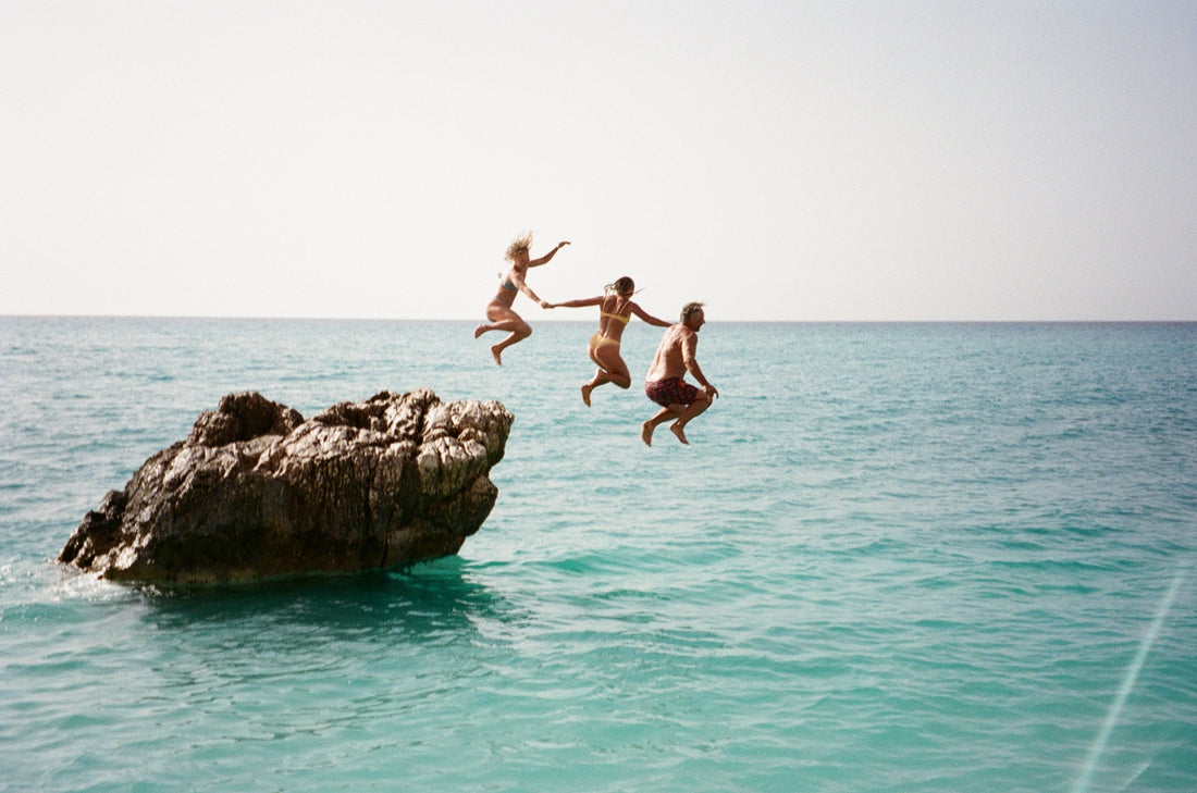 tři osoby skáčou do vody z kamene